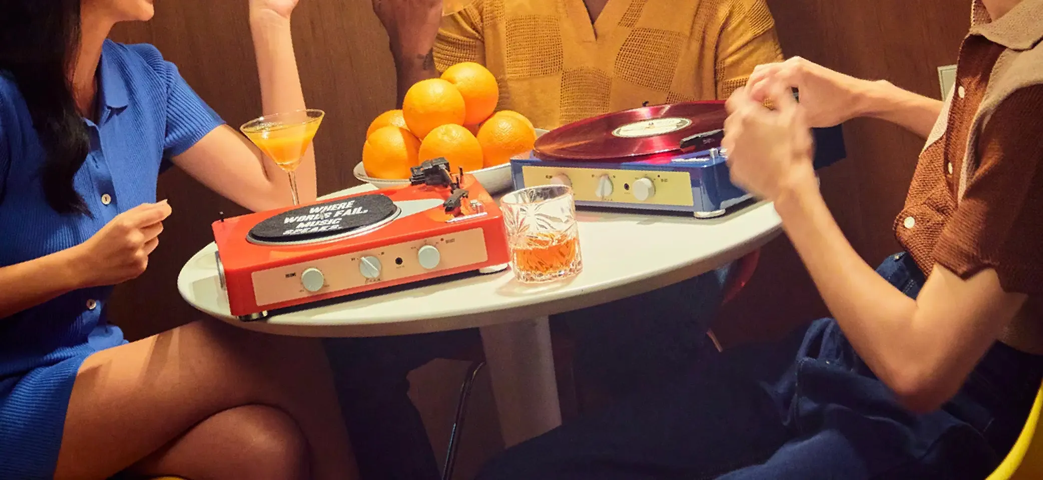 Gadhouse turntables spinning records on a cocktail table — friends sharing drinks and music